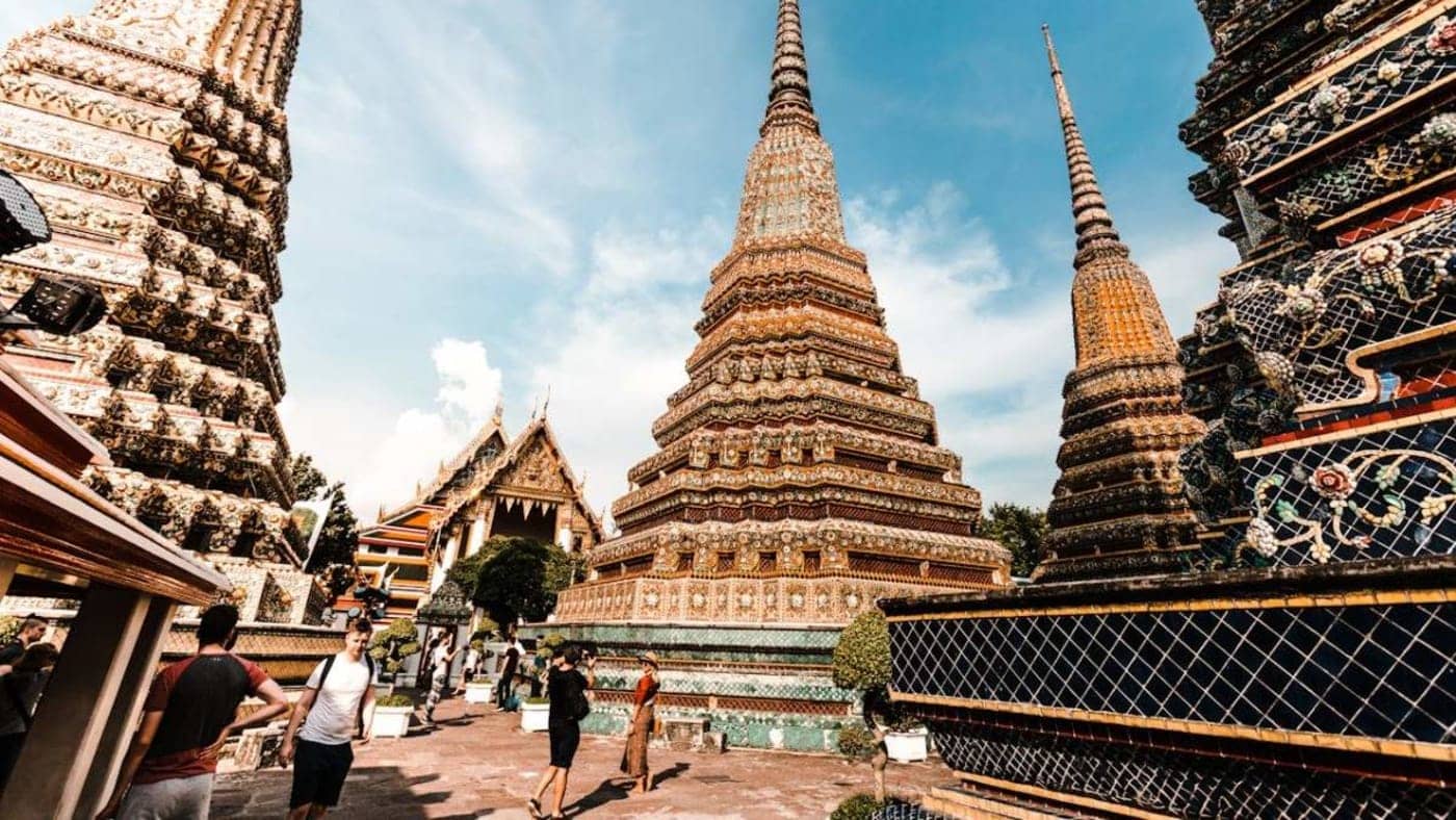 Visitors exploring ornate temple stupas and colorful architecture at Wat Pho in Bangkok during a tropical Thailand escape.