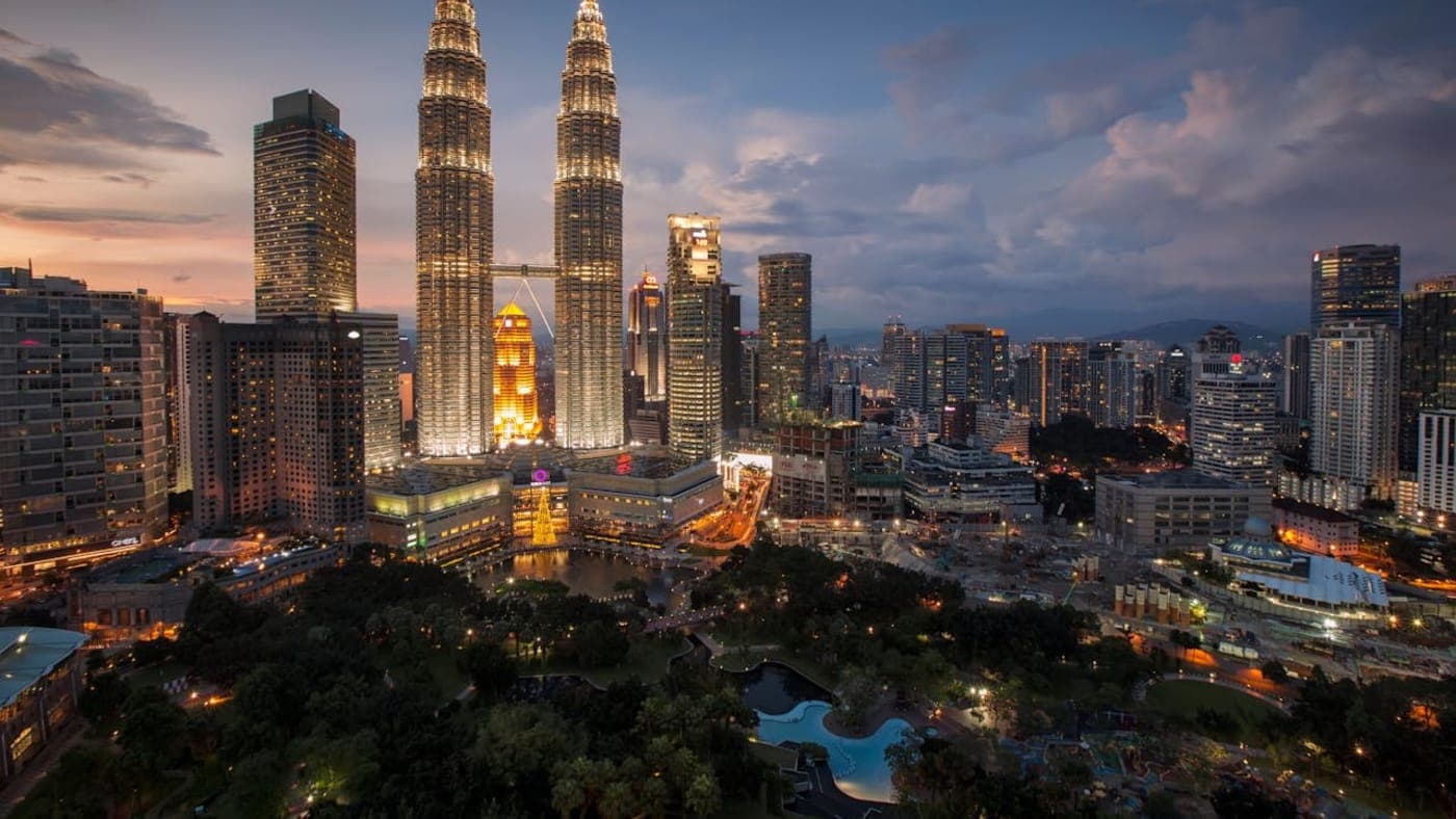 Petronas Twin Towers illuminated at dusk with Kuala Lumpur skyline and city lights in Malaysia.