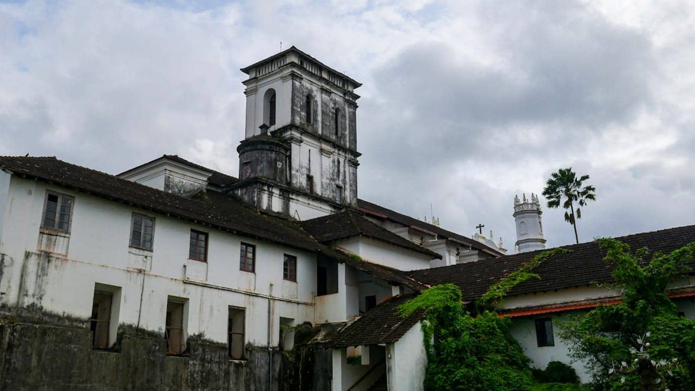 Historic Portuguese style church building with white walls and tower under cloudy sky in Goa, India.