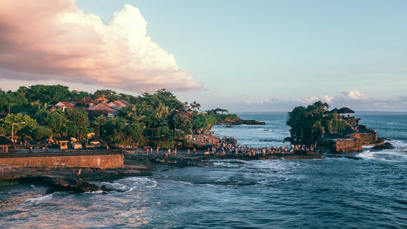 Tanah Lot sea temple on rocky island with ocean waves and sunset sky in Bali, Indonesia.