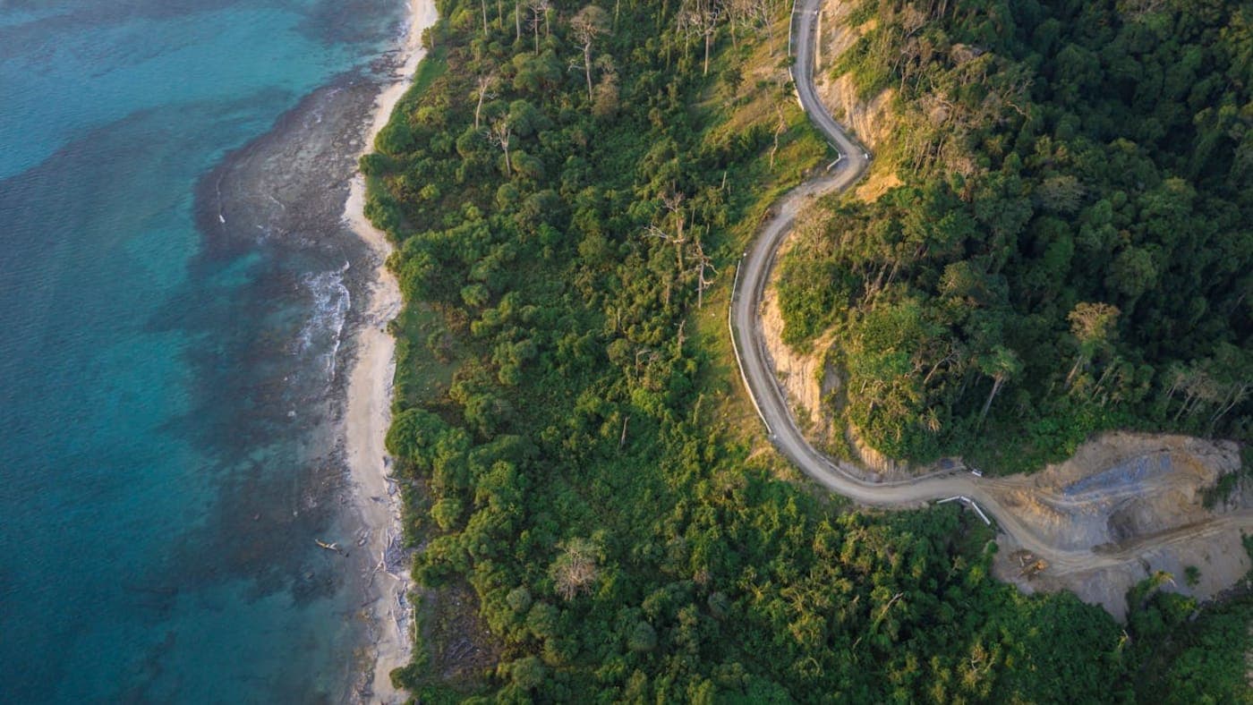 Winding coastal road through lush forest beside turquoise sea on Andaman Islands shoreline.