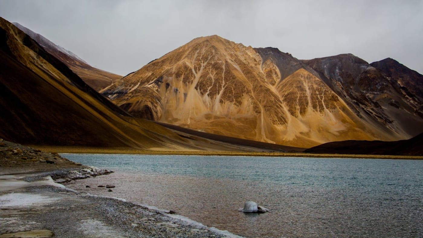 Pangong Lake with rugged brown mountains and clear blue water in the scenic landscape of Ladakh.