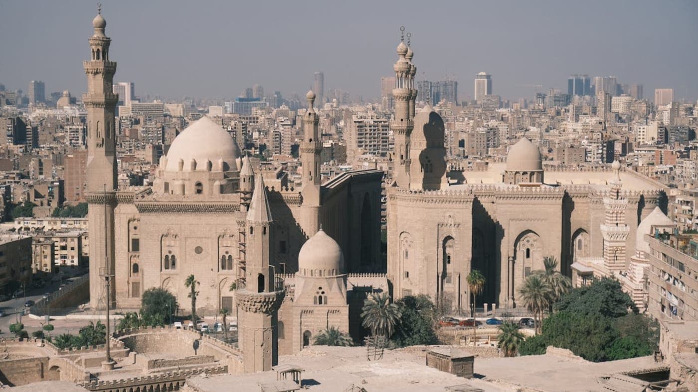 Historic mosque with domes and minarets overlooking Cairo skyline in Egypt.
