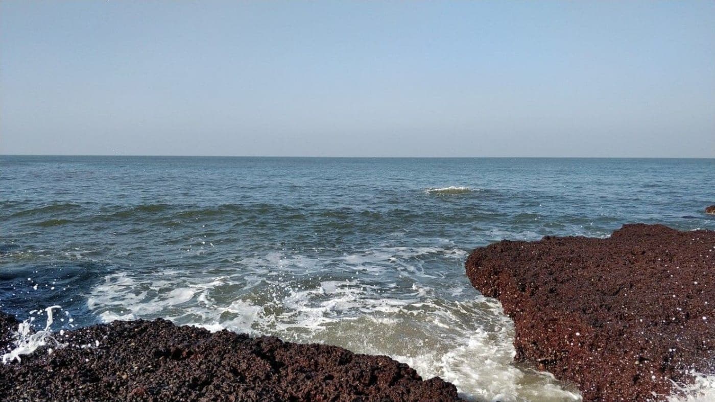 Waves crashing against rocky shoreline with open Arabian Sea horizon on scenic Goa coast.