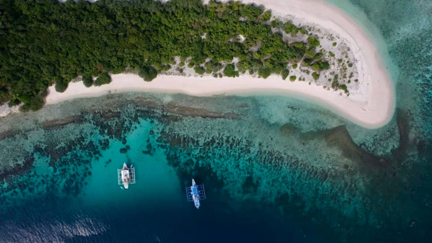 Aerial view of a small tropical island sandbar with clear blue water and boats in the Andaman and Nicobar Islands.