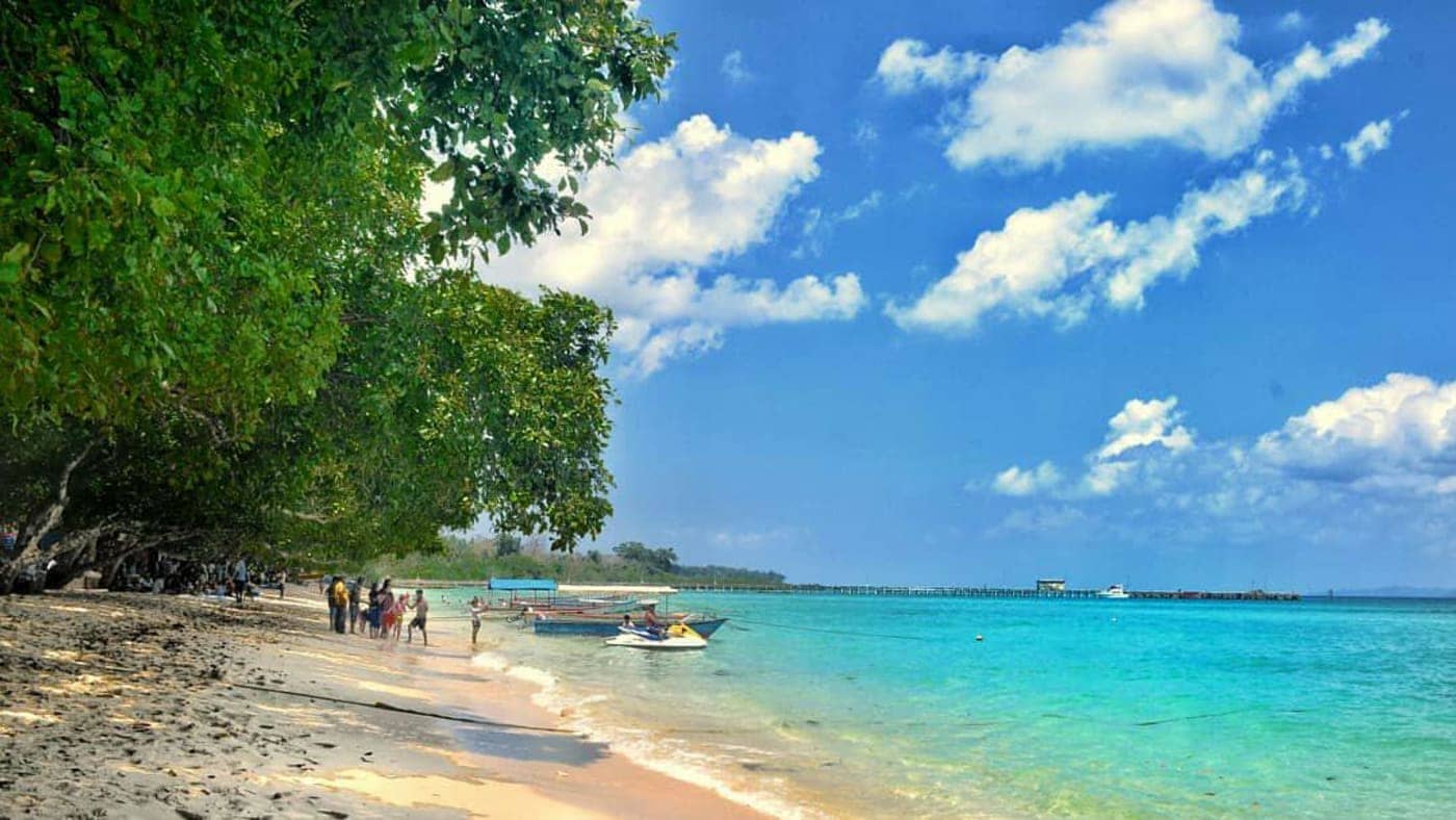 Tourists enjoying a tropical beach with boats and clear turquoise water in the Andaman and Nicobar Islands.
