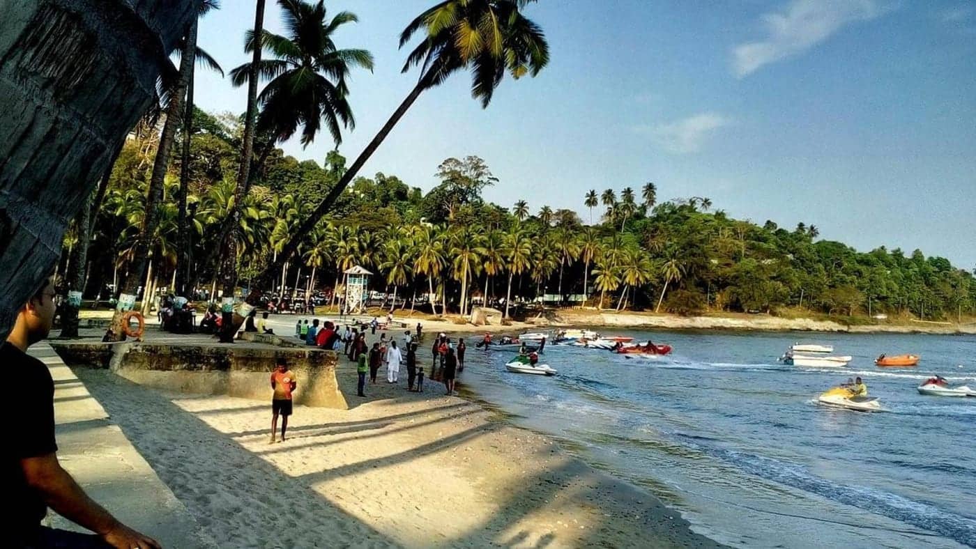 Visitors enjoying water activities and jet skis along a palm-lined beach in the Andaman and Nicobar Islands.