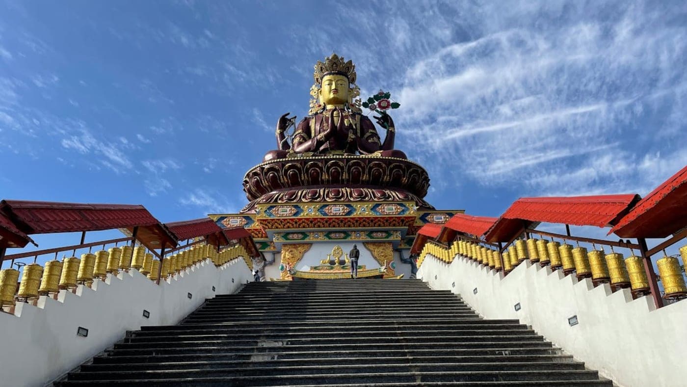Large Buddha statue in Sikkim atop a staircase with colorful monastery details under a clear blue sky
