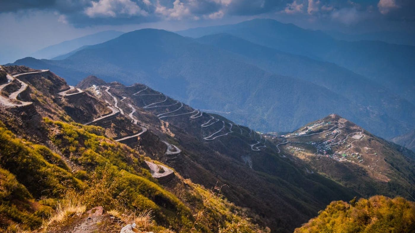Scenic Himalayan village beside a flowing river with colorful houses and snow-covered mountains in the background, Sikkim.