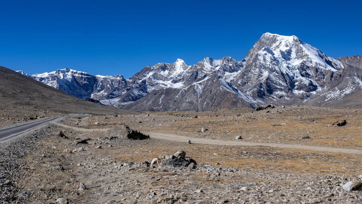 Snow-covered mountains in Sikkim with a winding road through a barren rocky landscape under a clear blue sky