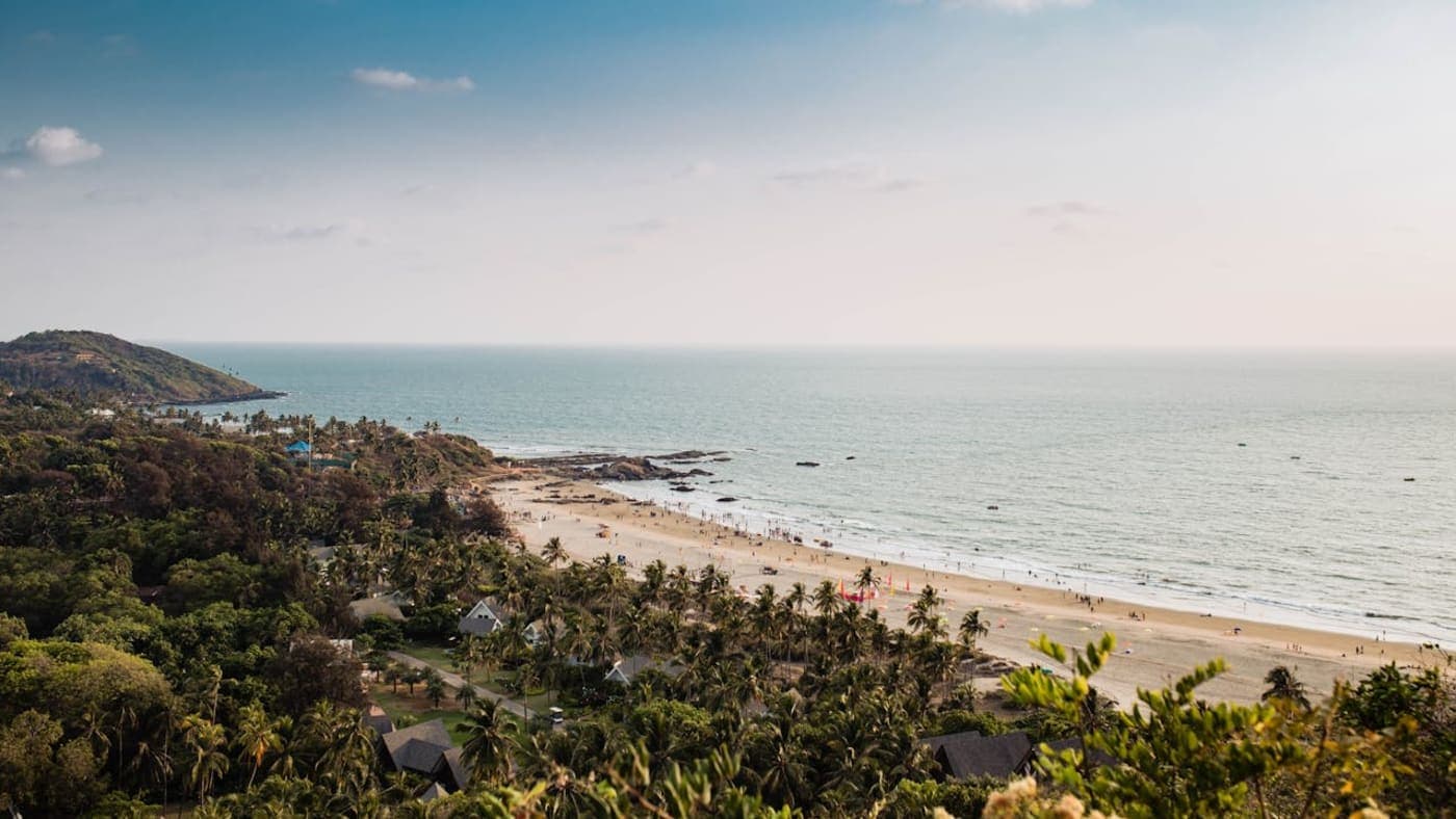 Sandy Goa beach with palm trees, waves, and tourists walking along the Arabian Sea shoreline.