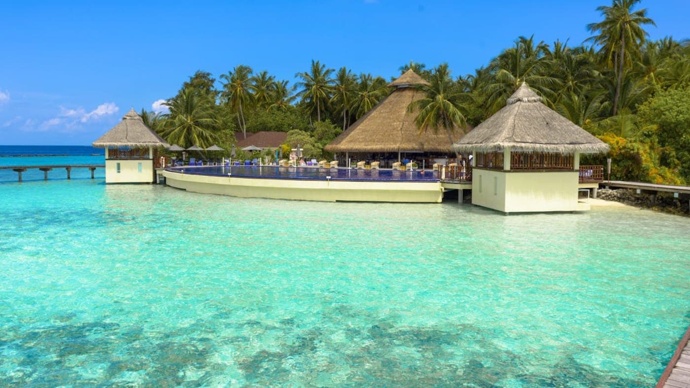 Wooden walkway leading to overwater bungalows on turquoise lagoon in the Maldives.