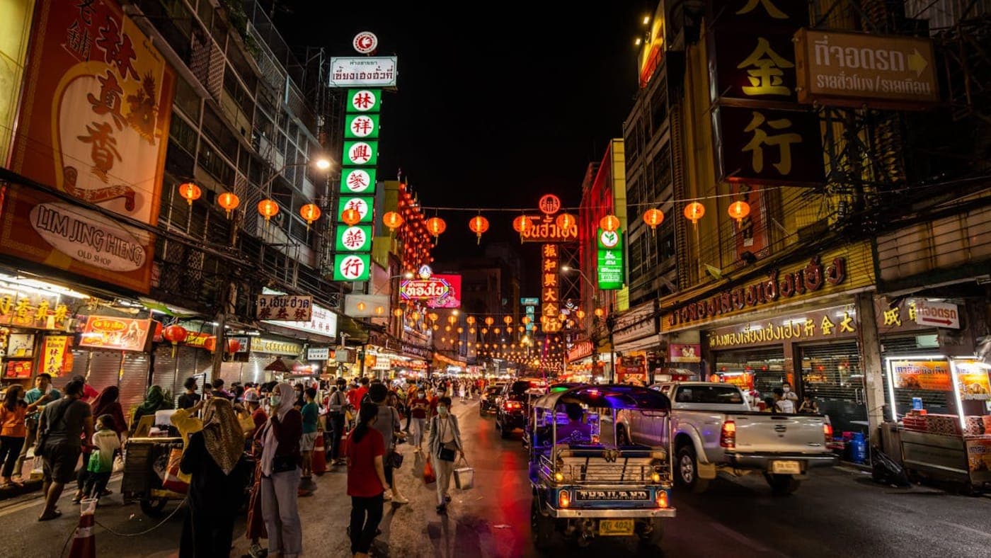 Longtail boats lined along a sandy beach in Krabi with turquoise water and towering limestone cliffs on a tropical island in Thailand.