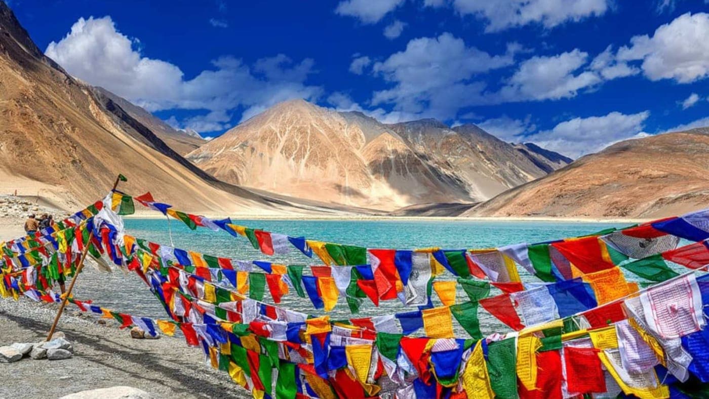 Colorful prayer flags over Pangong Lake in Ladakh with mountains and blue sky in the background