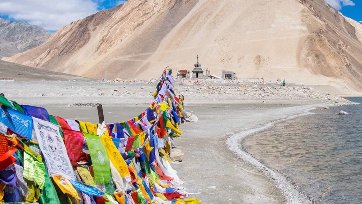 Colorful prayer flags along the shore of Pangong Lake in Ladakh with mountains and clear sky in the background