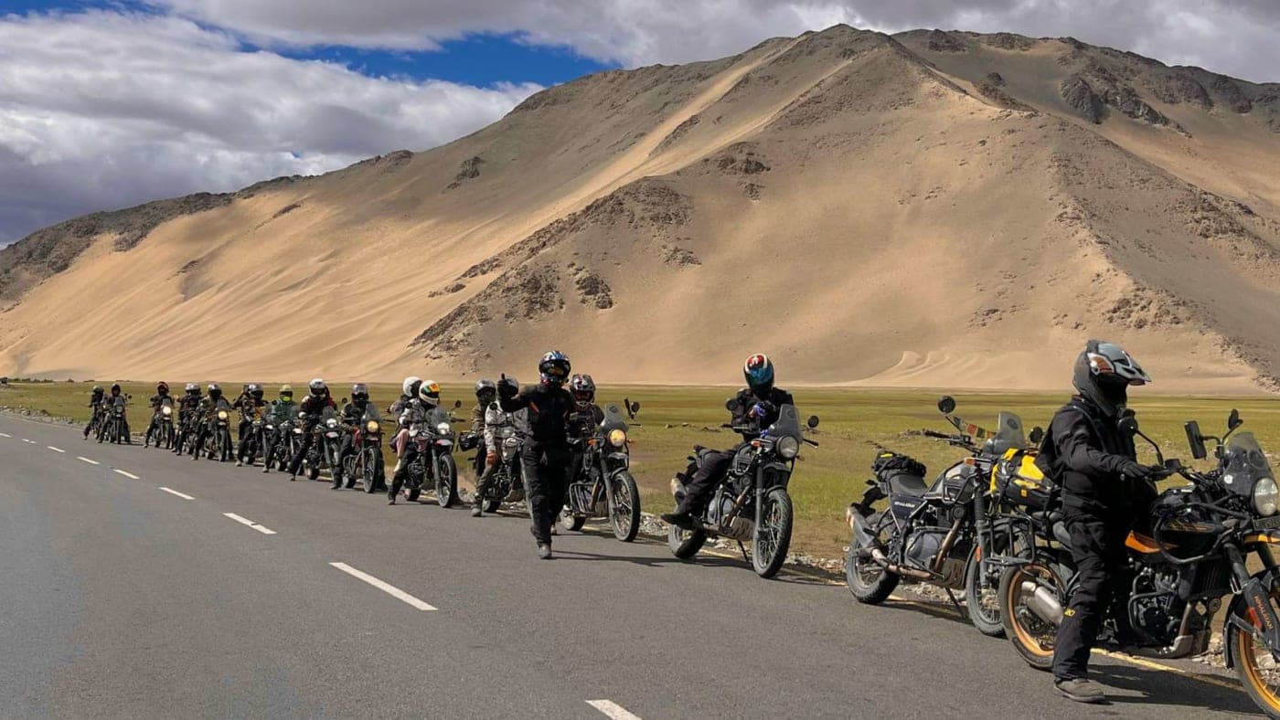 Group of bikers riding on a highway in Ladakh with mountains and dramatic cloudy sky in the background